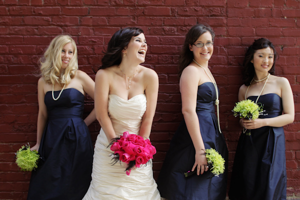 bride with brides maids - in black strapless dresses - laughing against a brick wall -photo by San Francisco based wedding photographer
